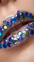 Closeup of lips adorned with multicolored rhinestones and glitter in shades of blue, purple, green and gold. Festive makeup look for special occasions, parties and celebrations.
