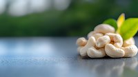 Raw cashew nuts scattered on dark surface with green leaf accent and soft natural lighting, creating appetizing composition for food photography and marketing.