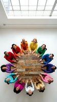 Diverse team of professionals in colorful clothing forming circle around wooden table in modern office space with natural lighting for teamwork concepts.