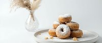 Fresh homemade donuts with sugar coating stacked on white plate, cozy kitchen setting with pampas grass decoration for bakery and food photography.