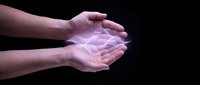 Cupped hands holding glowing geometric light formation with purple and pink illumination against dark background for spiritual and energy concepts.