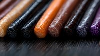Assorted makeup brushes with glitter eyeshadow tips in warm and cool tones arranged in a row on dark textured surface for cosmetics and beauty design projects.