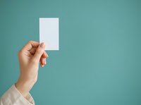 Hand holding blank white card on turquoise background, mockup for business cards, invitations, or promotional materials.
