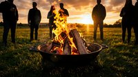 Group of friends gathering around crackling campfire at golden sunset in open field creating warm social atmosphere for outdoor adventure and bonding experience.