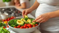 Pregnant woman in white dress preparing healthy salad with fresh vegetables, avocado and greens in modern kitchen. Healthy eating during pregnancy.