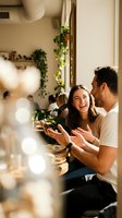 Happy young couple laughing together while cooking in modern kitchen with warm natural lighting and plants creating cozy domestic atmosphere.