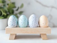 Speckled pastel Easter eggs on wooden display stand against light background, minimalist spring holiday decor in blue, mint, white and peach colors.