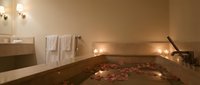 Luxury spa bathroom with romantic bathtub filled with rose petals and floating candles creating relaxing wellness atmosphere for self-care rituals.