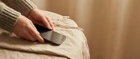 Woman in beige sweater using smartphone while relaxing on comfortable sofa at home. Modern lifestyle and digital communication concept for social media.