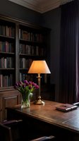 Elegant home library with wooden desk, brass table lamp, purple tulips and built-in bookshelves creating cozy reading atmosphere for luxury interior design.