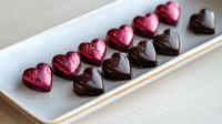 Heart-shaped chocolate candies and pink metallic bonbons arranged in line on white ceramic plate, romantic dessert for Valentine's Day celebration.