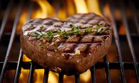 Juicy grilled beef steak with herbs and spices cooking on flaming barbecue grill, close-up view showing grill marks and caramelized surface.