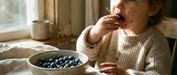 Toddler eating fresh blueberries from a bowl indoors, healthy snack for young children and nutrition.