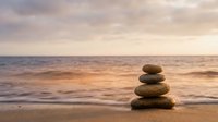 Balanced stone stack on sandy beach at sunset with calm ocean waves and golden sky creating peaceful meditation scene for wellness and mindfulness concepts.