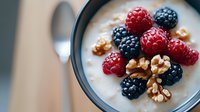 Fresh raspberries and blackberries with walnuts in creamy yogurt bowl, selective focus on berries against blurred background for food photography.