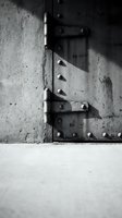 Old weathered metal hinge on concrete wall casting dramatic shadows in black and white monochrome photography for industrial design projects.