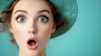Surprised young woman with bright blue eyes and open mouth wearing mint green hat against turquoise background, expressing astonishment and wonder.