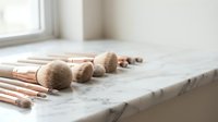 Set of professional makeup brushes with rose gold handles arranged on a marble surface near a bright window, beauty tools collection.