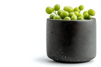 Fresh green peas in modern black concrete bowl with water drops on white background, minimalist food styling for restaurant menu and design.