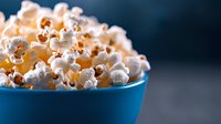 Fresh popcorn in bright blue bowl against dark background, dramatic lighting highlights white kernels and golden details, ready for movie night or snacking.