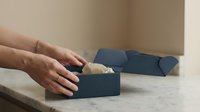 Hands opening elegant dark blue gift box on marble surface revealing surprise present inside for special occasion celebration.