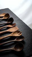 Handcrafted wooden spoons and fork arranged on dark slate surface. Natural wood grain texture. Eco-friendly kitchen utensils for sustainable cooking and dining.
