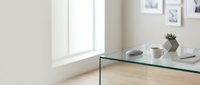 Modern minimalist glass coffee table with ceramic bowls and plant in bright contemporary living room with natural light and wooden floors.