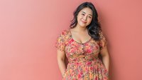 Young Asian woman in floral summer dress smiling confidently against coral pink background, representing body positivity and feminine fashion.