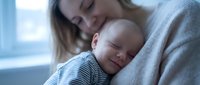 Young Caucasian mother gently holds her sleeping newborn baby, sharing a tender moment of love and bonding in soft natural light.