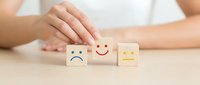 Hand protecting wooden blocks with emotional faces showing customer satisfaction and feedback concept for business service quality.