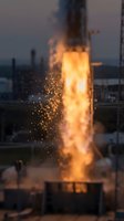 Massive industrial fire torch erupting with intense golden flames and glowing sparks against twilight sky, showcasing controlled combustion and energy release for engineering or manufacturing concepts.