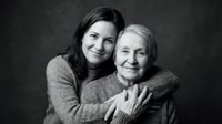 Middle-aged woman embracing elderly mother in warm hug against dark background. Black and white portrait showing intergenerational love and family bond.