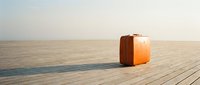 Vintage orange suitcase standing alone on a wooden boardwalk under a hazy sky, evoking travel, adventure, and solitude.