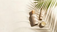 Luxury skincare products on sandy beach with tropical palm leaf shadow, natural sunlight. Summer beauty routine concept.