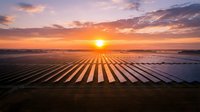Aerial view of solar panel farm at sunrise with golden sunlight reflecting off photovoltaic arrays, renewable energy generation and sustainable power infrastructure.