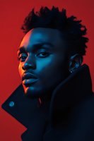 Young African American man with natural hair in dramatic blue and red lighting, wearing dark coat against vibrant red background for fashion or music promotion.