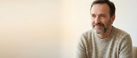 Middle-aged Caucasian man with gray beard wearing beige sweater, smiling at camera against neutral background. Portrait for business, lifestyle, and professional use.