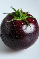 Fresh dark purple tomato with water droplets and green stem on white background, macro photography showing detailed texture and natural moisture.