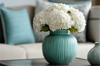 White hydrangea flowers in turquoise ribbed ceramic vase against soft interior background with matching decor elements create serene home atmosphere.
