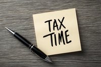 Tax time reminder written on yellow sticky note with black pen on wooden desk surface, concept for financial planning and tax season deadline.