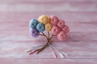 Delicate bouquet of pastel yarn balls arranged like flowers with twisted stems on pink textured background, creating soft and cozy crafting composition.