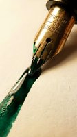 Vintage fountain pen with green ink on cream background, showing detailed brass nib and writing instrument for calligraphy, art, and design projects.