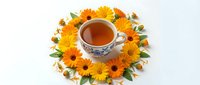 Herbal tea cup surrounded by fresh yellow and orange flowers with green leaves on white background, isolated for wellness and beverage design projects.