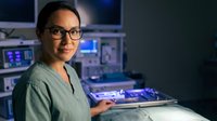 Asian female healthcare professional working night shift in modern hospital control room with medical monitoring equipment and digital displays.