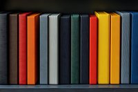 Colorful book spines arranged in row on dark shelf, showing minimal contemporary design aesthetic with vibrant hues against black background.