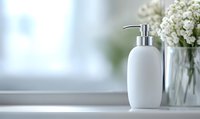 White ceramic soap dispenser on windowsill with fresh gypsophila flowers in glass vase against bright window background, minimalist bathroom decor composition.