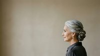 Mature woman with gray hair in side profile, wearing black clothing against neutral beige background. Suitable for senior lifestyle, aging gracefully, professional portraits.