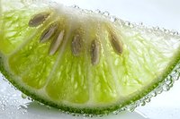 Fresh lime slice with water droplets in extreme macro view showing juicy pulp texture and citrus segments against bright background.