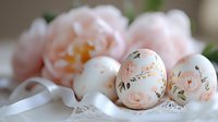 Delicate Easter eggs with hand-painted floral design in soft peach and pink tones, decorated with roses pattern, placed on white lace with satin ribbon.