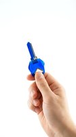 Hand holding blue house key on white background isolated for real estate and property concepts.